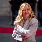 Giorgia Meloni in blazer grigio chiaro mentre posa sorridente sul red carpet.