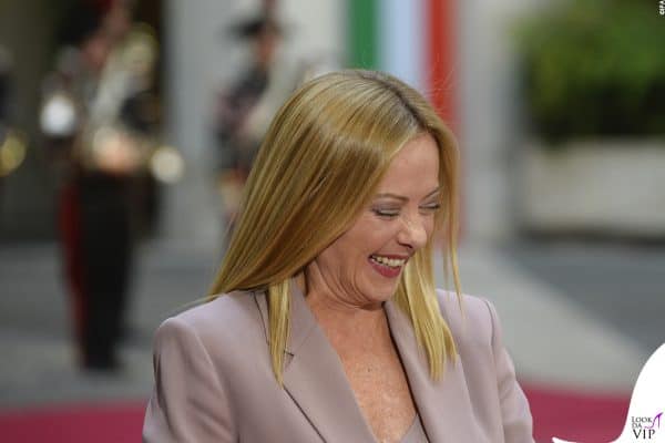 Look delicato per Giorgia Meloni che indossa un blazer cipria sorridendo davanti ai fotografi.